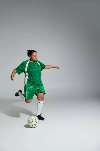 Una donna in uniforme da calcio verde prende a calci una palla in un ambiente da studio. — Foto stock