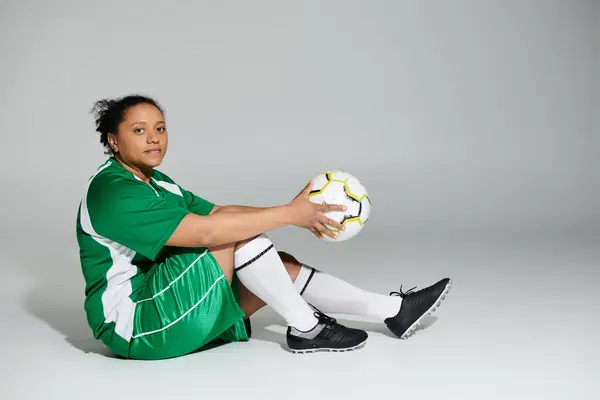 Una donna in uniforme da calcio verde si siede con un pallone da calcio in mano. — Foto stock