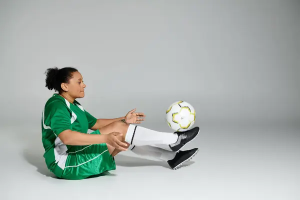 Donna in uniforme da calcio verde equilibra con grazia la palla sul piede disteso. — Foto stock
