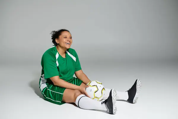 Donna sorridente in uniforme da calcio verde siede con la palla. — Foto stock