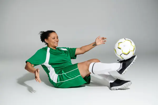 A woman wearing a green jersey and shorts juggles a soccer ball with her foot. — Stock Photo