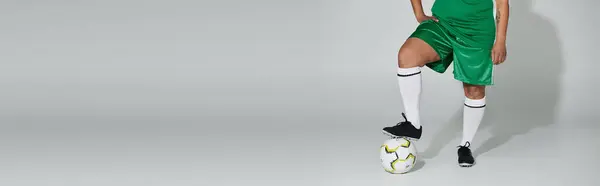 Un atleta donna in pantaloncini verdi e calzini bianchi in posa con un pallone da calcio. — Foto stock