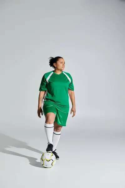 Uma mulher atlética em um uniforme de futebol verde dribla uma bola de futebol em um estúdio. — Fotografia de Stock