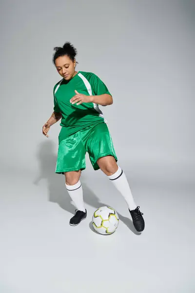 Uma atleta feminina em uma camisa verde dribla uma bola de futebol em um estúdio. — Fotografia de Stock
