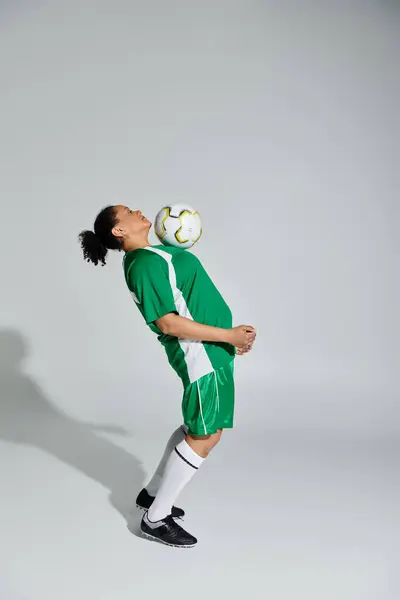 Una mujer con uniforme de fútbol verde y blanco hace malabares con una pelota en un estudio. - foto de stock