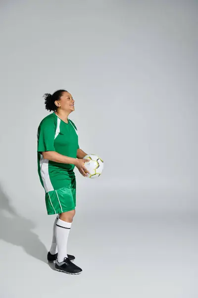 Una donna atletica in uniforme verde tiene un pallone da calcio, pronta a giocare. — Foto stock