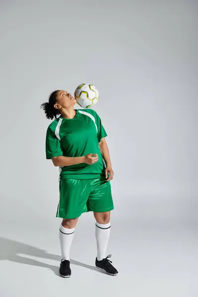 A woman in a green soccer uniform juggles a soccer ball with her head. — Stock Photo