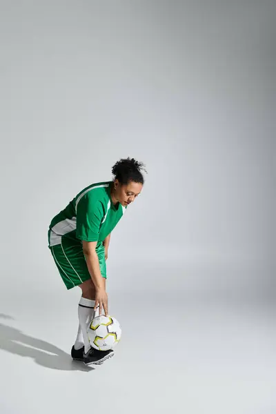 An athletic woman in green soccer uniform bends down, ready to pass the ball. — Stock Photo