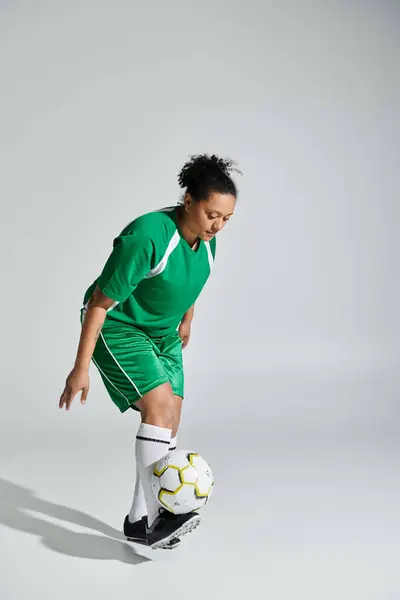 A female soccer player in a green jersey and shorts juggles a soccer ball in a studio setting. — Stock Photo