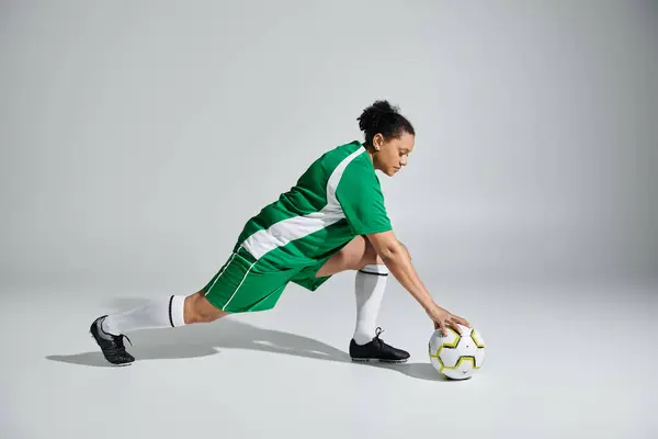 Female athlete in green jersey stretching on white studio floor, reaching for soccer ball. — Stock Photo
