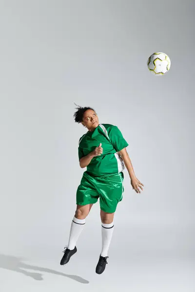 A female athlete in a green soccer uniform leaps to catch the ball mid-air. — Stock Photo