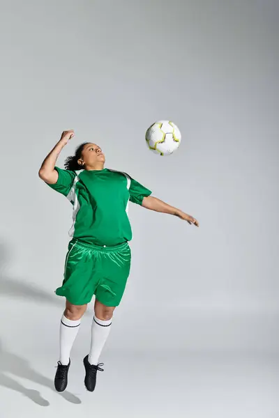 Un'atleta donna in uniforme da calcio verde salta in aria per dirigere un pallone da calcio. — Foto stock