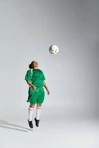 Женщина в зеленой футбольной майке прыгает в воздухе, чтобы возглавить футбольный мяч. — стоковое фото