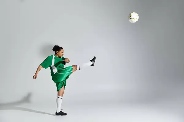 Una donna che indossa un'uniforme da calcio verde prende a calci un calcio in un ambiente da studio. — Foto stock