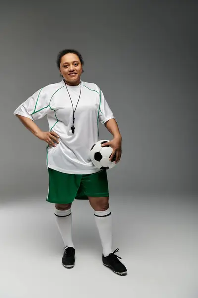 A woman in a referee uniform stands confidently, holding a soccer ball. — Stock Photo