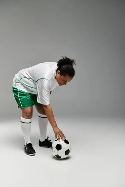Female athlete in white jersey and green shorts prepares for football, hand reaching for ball. — Stock Photo