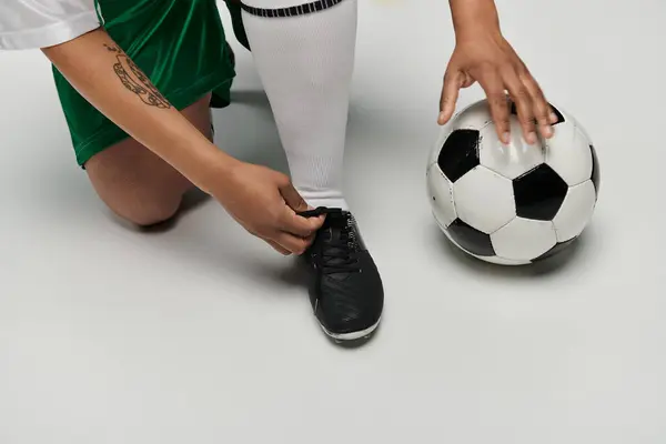 Una donna in uniforme verde e bianca si lega le scarpe prima di una partita di calcio. — Foto stock