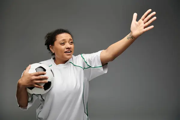 Eine Frau im weißen Trikot hält einen Fußballball in der Hand und lächelt zur Seite. — Stockfoto