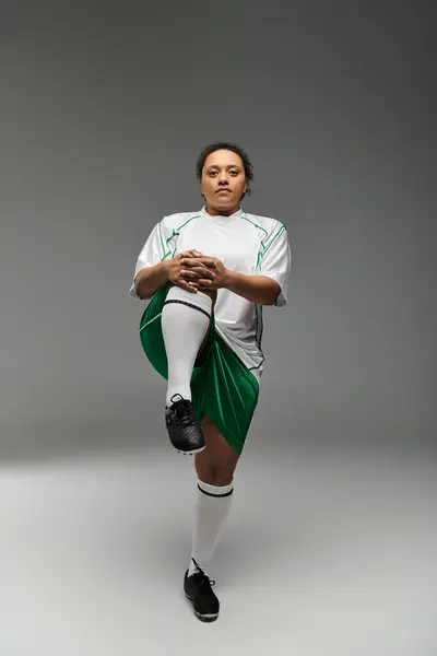 A female athlete in a white and green jersey stretches her leg before a football game. — Stock Photo
