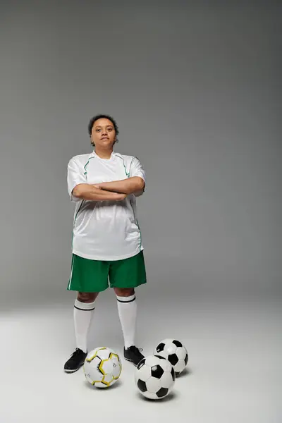 Una donna in uniforme da calcio si alza con le braccia incrociate, circondata da palloni da calcio. — Foto stock