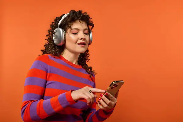 Una joven con el pelo rizado posa en un suéter a rayas de colores sobre un fondo naranja brillante. — Stock Photo
