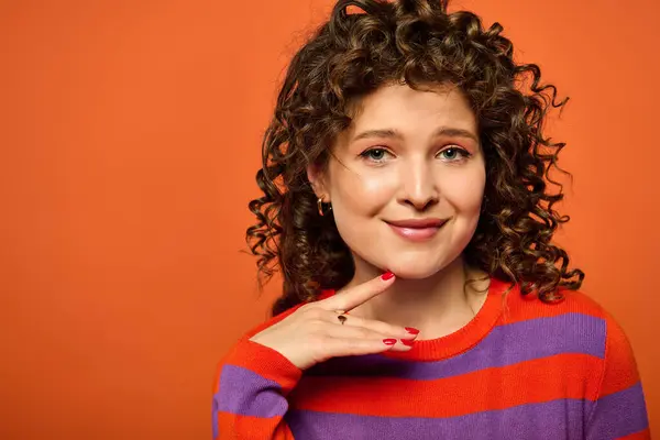 Eine junge Frau mit lockigem Haar posiert selbstbewusst in einem gestreiften Pullover vor leuchtend orangefarbenem Hintergrund. — Stockfoto