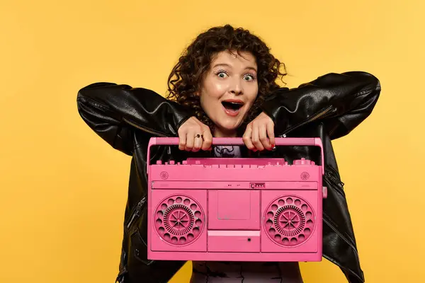 Lächelnde Frau mit lockigem Haar in schwarzer Lederjacke hält rosa Boombox in die Kamera. — Stockfoto