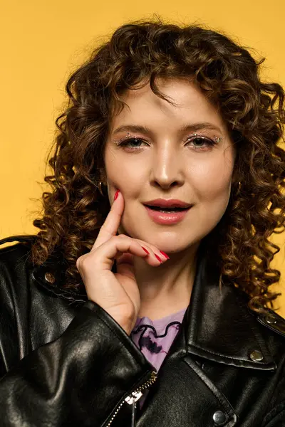 Uma jovem elegante com cabelo encaracolado posa em uma jaqueta de couro preto contra um fundo amarelo brilhante. — Fotografia de Stock