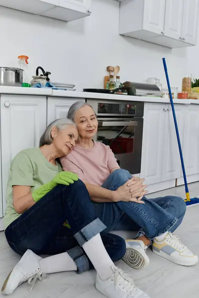 A mature lesbian couple sits together in a modern kitchen after finishing their cleaning tasks. — Stock Photo