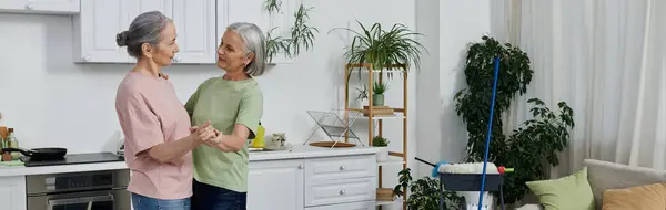 A mature lesbian couple cleans their modern apartment together, showcasing a loving connection amidst everyday tasks. — Stock Photo