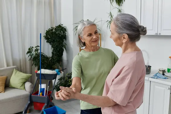 Um casal de lésbicas mais velhas limpa seu apartamento moderno juntos, rindo e desfrutando uns dos outros companhia. — Fotografia de Stock