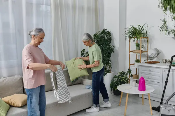 Duas mulheres, em uma relação lésbica, arrumam seu apartamento moderno, uma segurando um travesseiro e a outra dobrando um cobertor. — Fotografia de Stock