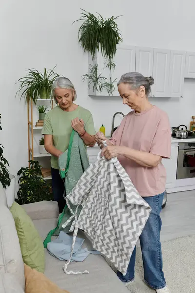 Zwei reife lesbische Frauen falten Wäsche in ihrer modernen, hell erleuchteten Wohnung. — Stockfoto