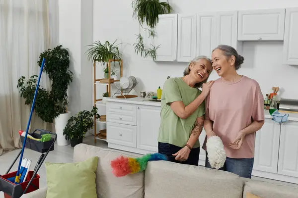 Um casal lésbico ri juntos enquanto limpa seu apartamento moderno. — Fotografia de Stock