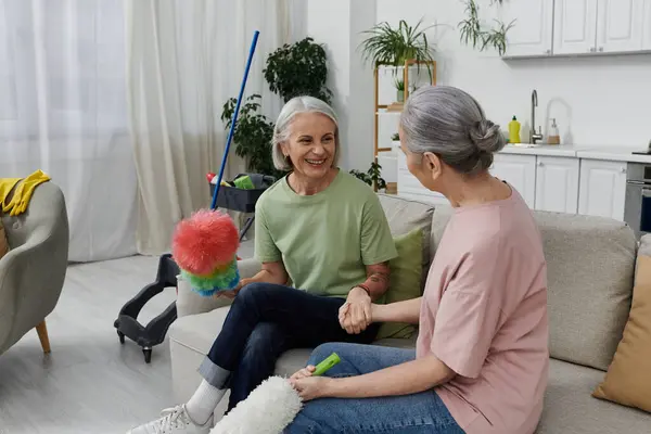 Two mature women, a lesbian couple, are cleaning their modern apartment together. They are laughing and enjoying each others company. — Stock Photo