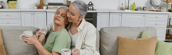 A mature lesbian couple relaxes on a couch in their modern apartment, enjoying a moment of peace after cleaning. — Stock Photo