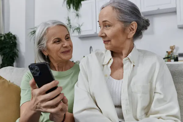Zwei ältere Frauen, ein lesbisches Paar, entspannen sich auf einer Couch mit Telefon in einer modernen Wohnung — Stockfoto