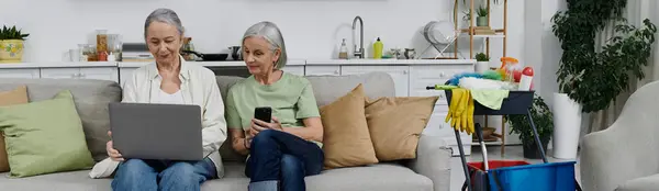 Two mature women relax on a couch in their modern apartment after a day of cleaning. — Stock Photo