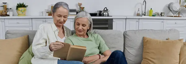 Una coppia lesbica matura si rilassa su un divano nel loro appartamento moderno, condividendo un libro — Foto stock