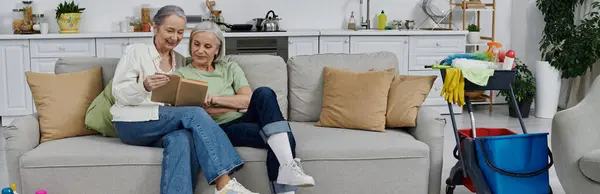 A mature lesbian couple relax on their sofa after cleaning their modern apartment together. — Stock Photo