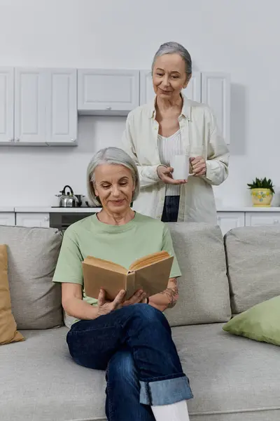 Lgbt couple relaxing on a modern couch after cleaning. One reads while the other enjoys tea in their apartment. — Stock Photo