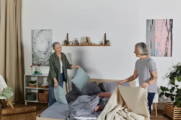 Zwei reife lesbische Frauen machen ihr Bett zusammen in einer modernen Wohnung. — Stockfoto