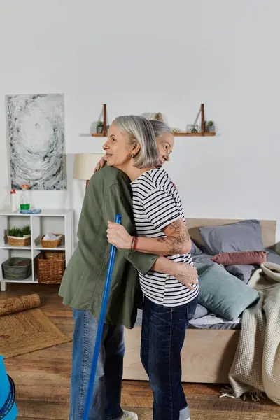 Um casal lésbico em traje casual abraça enquanto limpa seu apartamento moderno. — Fotografia de Stock
