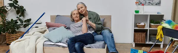 A mature lesbian couple relaxes on a bed in their modern apartment, taking a break from cleaning. — Stock Photo