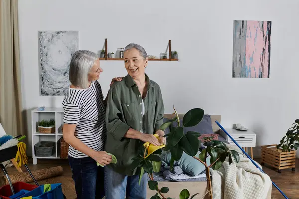 A mature lesbian couple cleans their apartment together, laughing and enjoying each others company. — Stock Photo