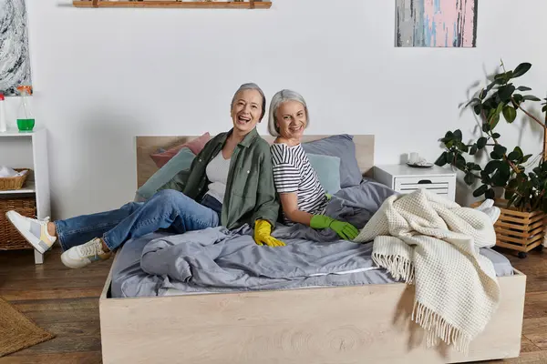 Duas mulheres lésbicas maduras limpando seu apartamento moderno juntas, sorrindo e rindo na cama. — Fotografia de Stock