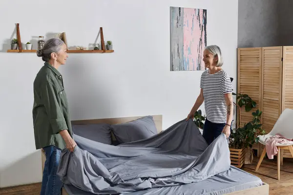 Una pareja lesbiana en atuendo casual hace la cama juntos en su apartamento moderno. — Stock Photo