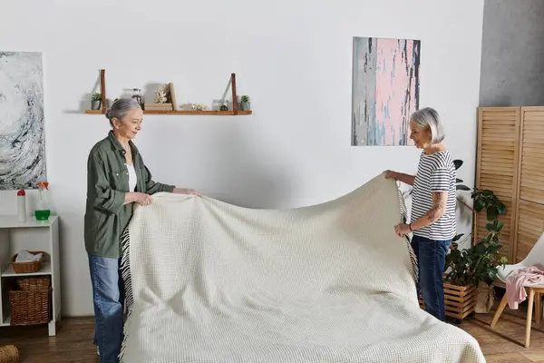 Duas mulheres lésbicas maduras em traje casual fazem a cama juntas em seu apartamento moderno. — Fotografia de Stock