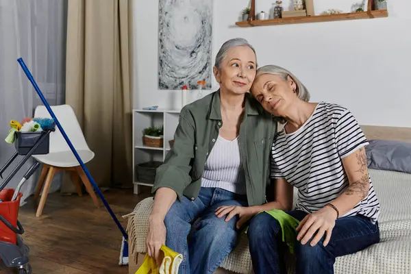 Duas mulheres lésbicas maduras fazem uma pausa de limpar seu apartamento moderno, descansando juntas no sofá. — Fotografia de Stock