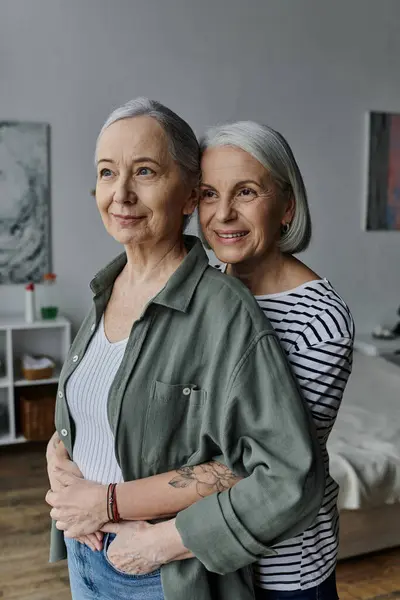 A mature lesbian couple embraces in a modern apartment, their smiles reflecting a lifetime of love and companionship. — Stock Photo